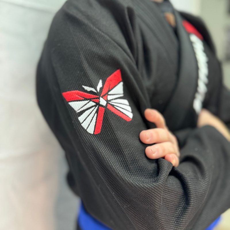 Sleeve of a black ButterflyX gi with the butterfly logo and a blue belt