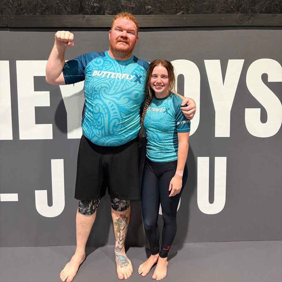 Two people on the mats in matching custom teal ButterflyX rash guards with a tribal pattern